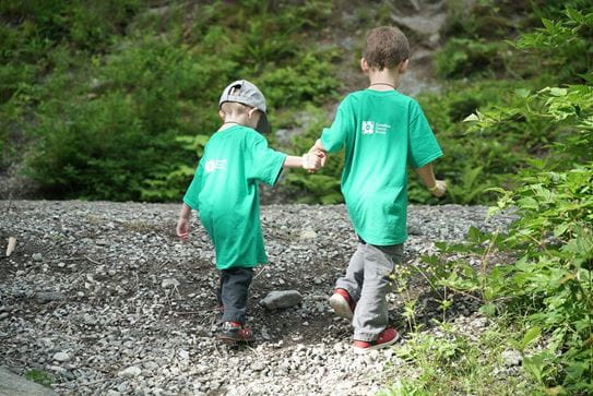 Deux petits garçons portant les tshirts verts de la Société canadienne du cancer, se tenant par la main et marchant dans la nature. 
