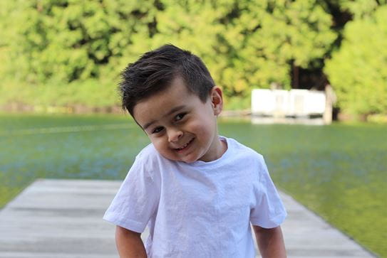 A little boy smiling on a dock at a lake.