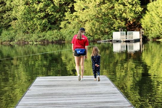 A camper and staff member walking along a dock towards a lake.