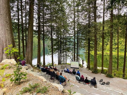 Families watching a movie on a projector outside in a forest.