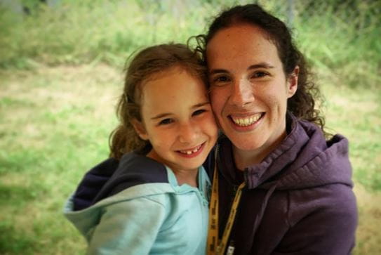 A woman and little girl side by side smiling.