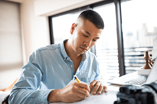 Un homme assise à un bureau écrit dans un cahier de notes.