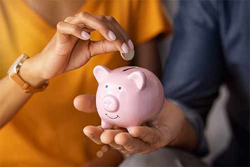 A woman and man putting a coin in a piggy bank.