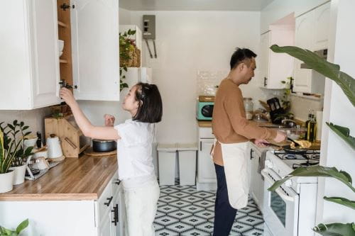 A woman opening the kitchen cabinet and man cooking.