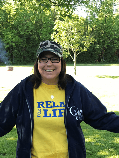 Dianne debout à l’extérieur, portant un t-shirt et un chandail à capuchon du Relais pour la vie.