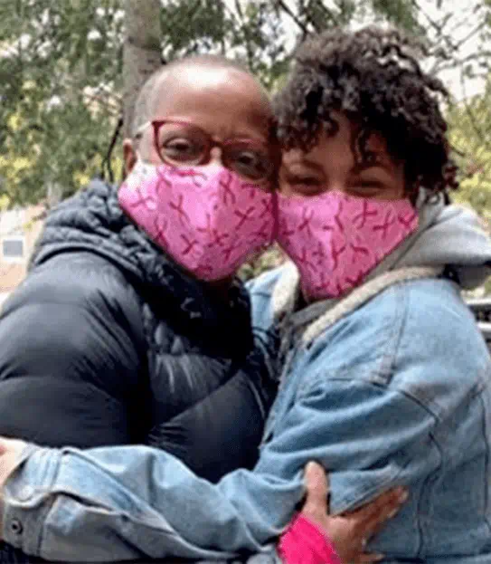 Coral tient dans ses bras sa fille, adulte, et elles portent toutes deux des couvres-visages réutilisables roses.