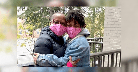 Coral hugging her adult daughter, while they’re both wearing pink face masks.