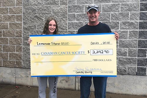 Cassidy and her dad smiling holding up a large cheque with the funds raised from her lemonade stand.