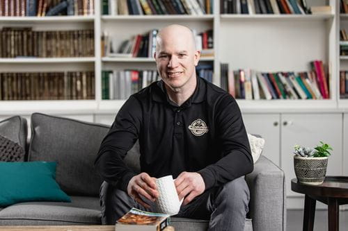 A smiling man sitting on a sofa holding a coffee cup in his hands.