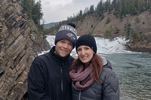 A man and woman standing in front of a river smiling.