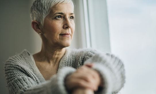 An older woman sitting in a dimly lit room, looking out the window,