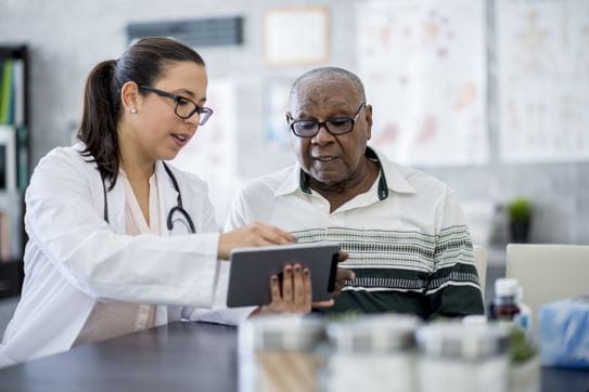 An older man reviewing test results on a tablet with a female doctor.