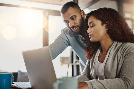 A couple sitting at a table looking at a laptop.