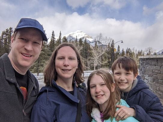 The Bradley family smiling outside on a winter day, with trees and mountains in the background.