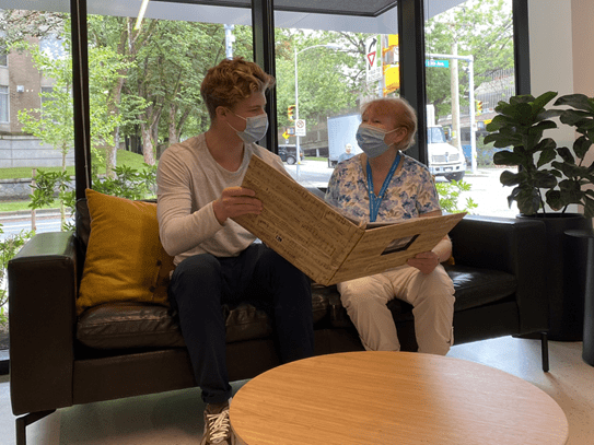 Owen sitting in a lounge area with another volunteer looking at a book of music together.