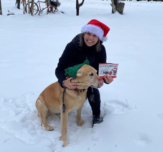 Kim wearing a Santa hat, knelling by her dog.