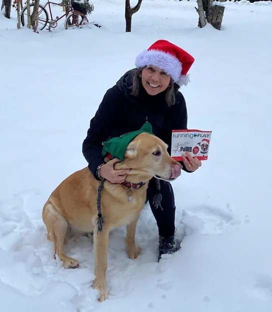 Kim wearing a Santa hat, knelling by her dog.