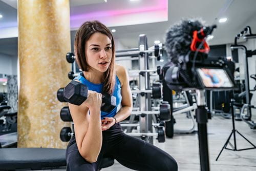Une femme filme sa séance de musculation dans une salle de sport.