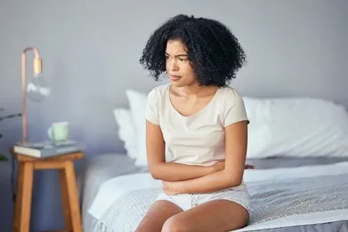 A person sitting on her bed, holding her stomach and looking worried