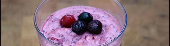 A fruit smoothie in a glass with berries set on top as a garnish