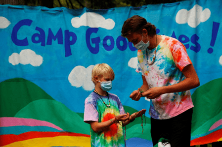 A Camp Goodtimes counsellor making a necklace with a camper.
