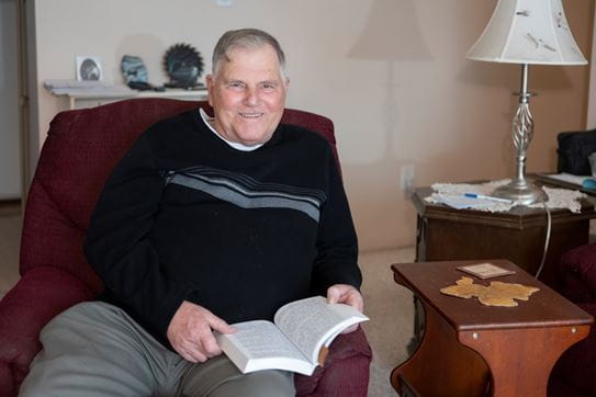 Warren Waseen sitting in an armchair with a book in his lap.