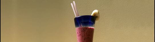 A fruit smoothie in a glass with a slice of banana on the rim.