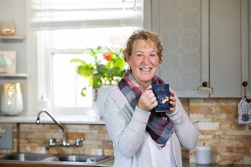 Cindy Goguen, holding a coffee mug and laughing in a kitchen.