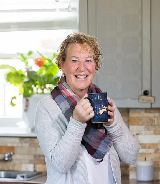 Cindy Goguen, holding a coffee mug and laughing in a kitchen.