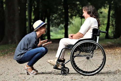 A person talking and laughing with a person in a wheel chair.