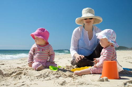 A parent with two babies on the beach.