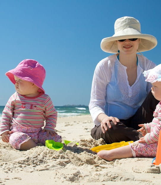 A parent with two babies on the beach.