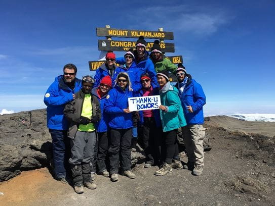 Jeff with a group of 10 friends and CIBC employees at the top of Mt. Kilimanjaro, holding a sign that reads “Thank-U Donors”.