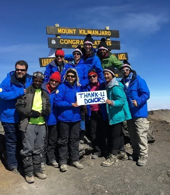 Jeff with a group of 10 friends and CIBC employees at the top of Mt. Kilimanjaro, holding a sign that reads “Thank-U Donors”.