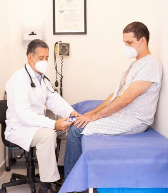 A person in a hospital gown sitting on an exam table being examined by a doctor
