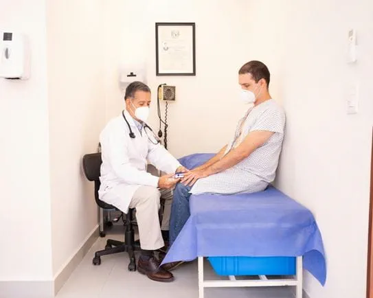 A person in a hospital gown sitting on an exam table being examined by a doctor