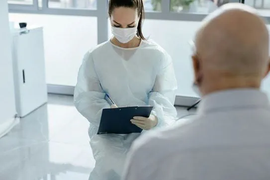 A doctor sitting in front of a person and writing on a clipboard