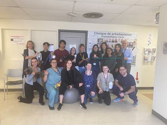Dr Chelsia Gillis and her team are holding exercise equipment in a hallway outside a closed door and a bulletin board.