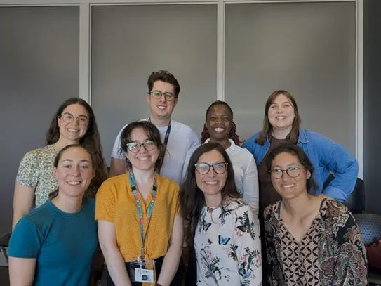 Dr Corentin Montiel and his team are standing in front of a grey wall with white vertical panels in 2 rows.