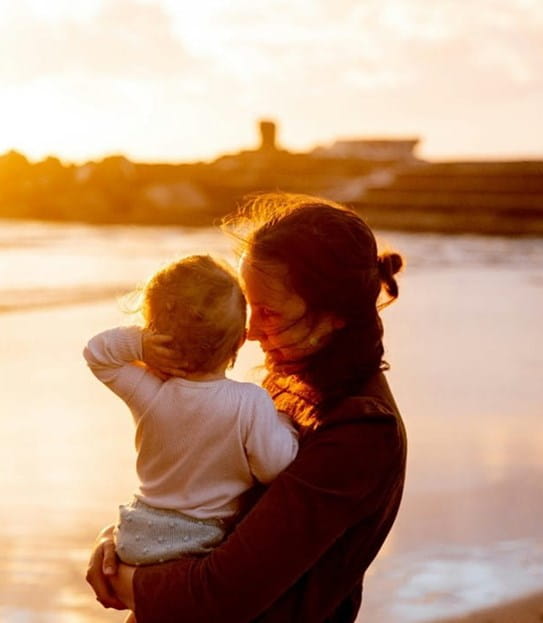 Une personne tenant un enfant sur une plage.