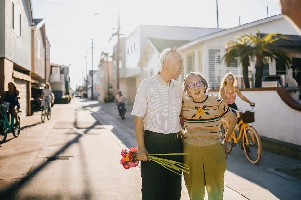 A couple walking down a street on a sunny day. Several people riding bikes are behind them.