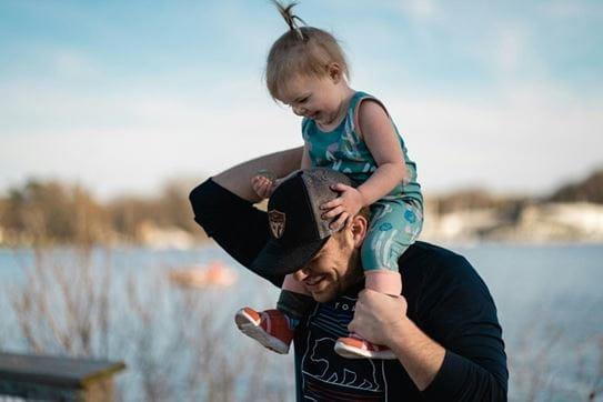 Un enfant monté sur les épaules d’une personne au bord d’un lac.