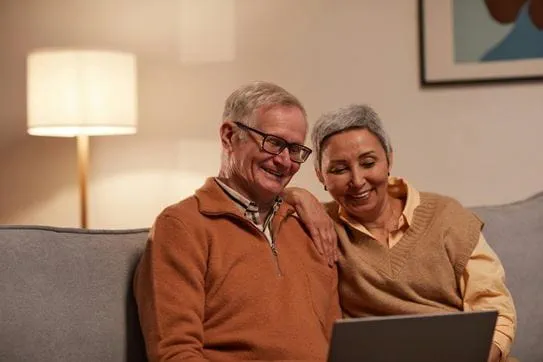 Two people sitting on a couch, looking at a laptop and smiling.