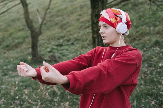 Une personne portant un fichu de tête dans un parc, en train de faire des étirements avec ses bras.