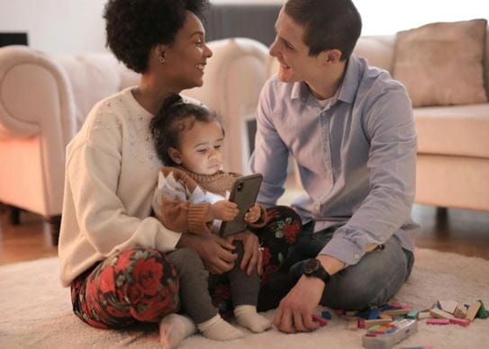 Two parents smiling at each other while sitting with their baby