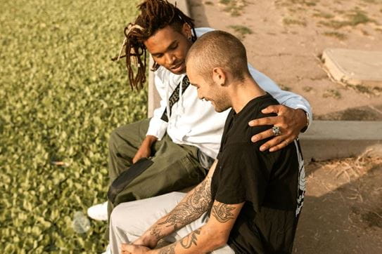 A person with his arm around his friend’s shoulders while they both sit