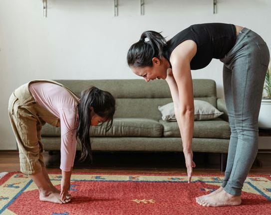 A woman and girl facing each other and reaching for their toes