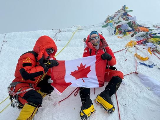 Meredith holding a Canadian flag with another person, sitting on some snow.