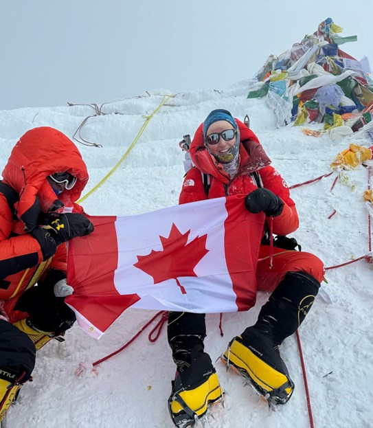 Meredith et une autre personne, assises dans la neige en tenant un drapeau canadien
