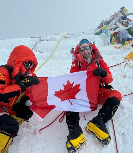Meredith holding a Canadian flag with another person, sitting on some snow.